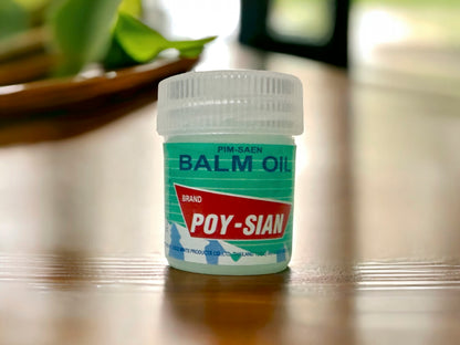 A small, cylindrical container labeled 'BALM OIL' by Poy-Sian, placed on a table with a plant in the background.